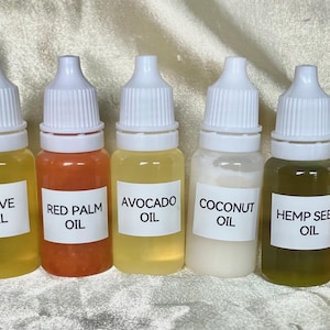 May include: A row of ten small clear bottles with white caps and labels. Each bottle contains a different colored oil, including sesame, sunflower, olive, red palm, avocado, coconut, hemp seed, walnut, salmon, and peanut oil.
