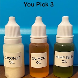 May include: Three small bottles with white caps and labels. The bottles contain coconut oil, salmon oil, and hemp seed oil. The text "You Pick 3" is above the bottles.