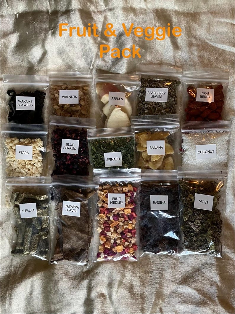 May include: A collection of clear plastic bags filled with various dried fruits, vegetables, and herbs. The bags are labeled with names like "Apples," "Blue Berries," and "Spinach." The text "Fruit & Veggie Pack" is at the top.
