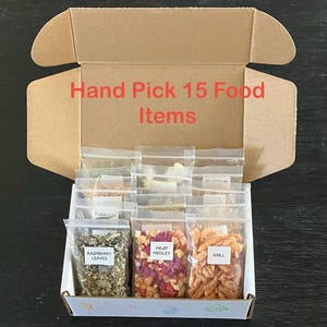 May include: An open cardboard box filled with 15 small, clear plastic bags of food items. The bags are labeled with names like "Raspberry Leaves," "Fruit Medley," and "Krill." The box has the text "Hand Pick 15 Food Items" in red.