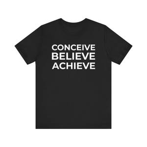 Puede incluir: Camiseta negra con las palabras "CONCEIVE BELIEVE ACHIEVE" impresas en blanco, apiladas verticalmente. La camiseta tiene mangas cortas y cuello redondo.