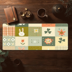 May include: A rectangular desk mat with a patchwork design featuring squares with floral, bunny, and clover motifs in shades of green, orange, and white. The mat is on a dark wooden surface.
