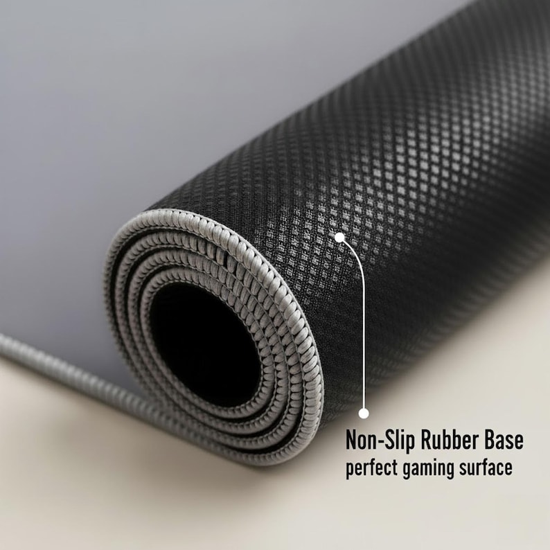 May include: Rolled-up gray and black gaming mouse pad. The mouse pad has a non-slip rubber base and a textured surface. The edge is stitched with gray thread. Text on the image reads: Non-Slip Rubber Base perfect gaming surface.