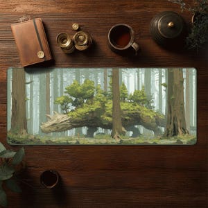 Puede incluir: Una alfombrilla de ratón rectangular con una escena de bosque de fantasía con una criatura parecida a un dragón cubierta de árboles y follaje. El fondo muestra un bosque brumoso con árboles altos. La alfombrilla está rodeada por un cuaderno de cuero marrón, una taza de té y otros accesorios.