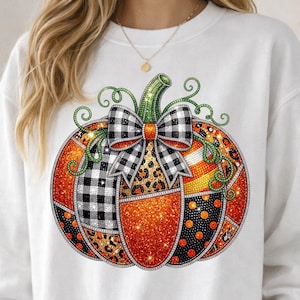 May include: A white crewneck sweatshirt featuring a large graphic of a pumpkin. The pumpkin is divided into sections with various patterns including black and white buffalo plaid, leopard print, orange glitter, and black with orange polka dots.