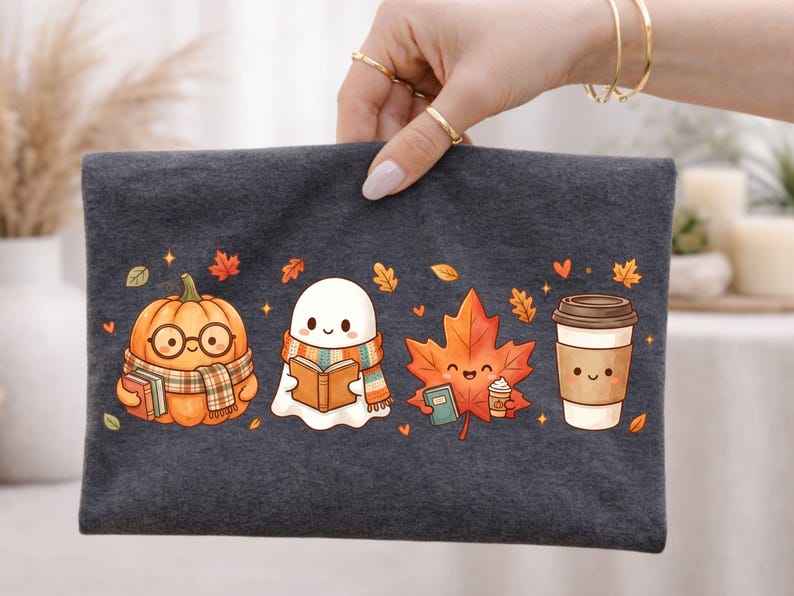 May include: A dark gray fabric pouch featuring a colorful graphic print of a smiling pumpkin wearing glasses and a scarf, a ghost reading a book, a maple leaf holding a small book and coffee cup, and a disposable coffee cup with a smiling face.