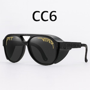 Puede incluir: Gafas de sol negras con letras doradas "PIT VIPER" y "CC6" en la parte superior. Las gafas de sol tienen un dise&ntilde;o &uacute;nico con protectores laterales y un puente. Las lentes son oscuras y las monturas negras.