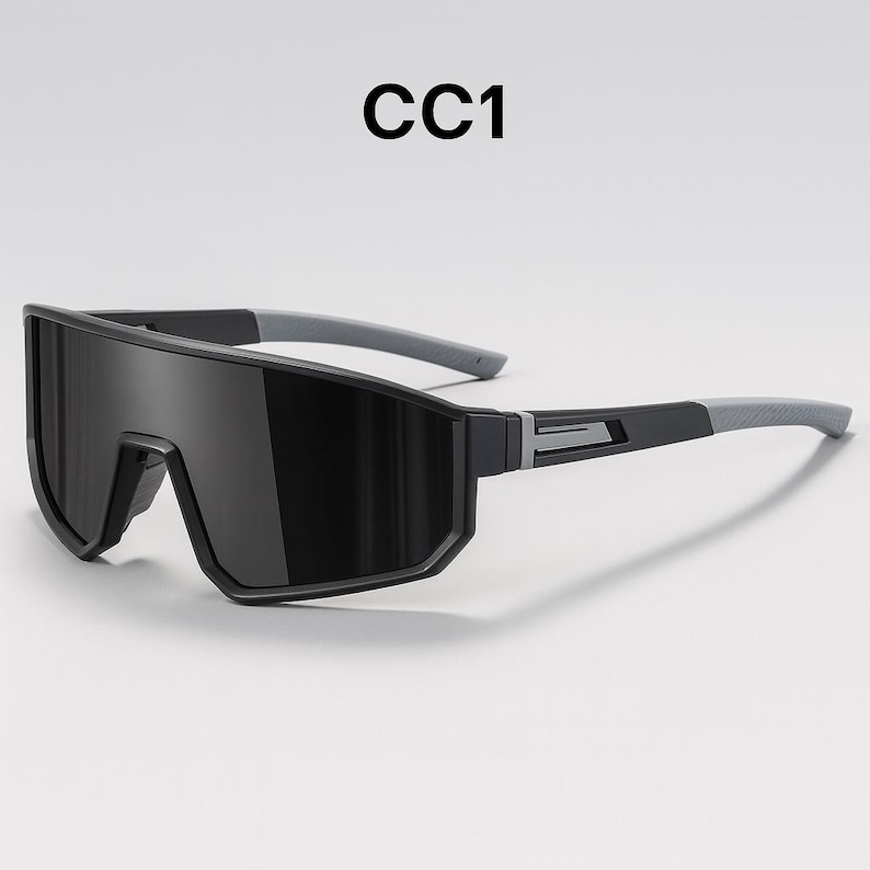 May include: Black sport sunglasses with a wraparound design. The sunglasses have a thick, black frame with gray temples. The text "CC1" is printed in black at the top of the image. The lenses are dark, providing full coverage.