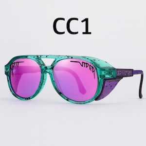Puede incluir: Gafas de sol verdes y moradas con lentes rosas. Las gafas tienen un dise&ntilde;o &uacute;nico con puente y protectores laterales. El texto "CC1" est&aacute; impreso en la parte superior. Las lentes son espejadas y las monturas son de color verde transl&uacute;cido.