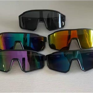 May include: Collection of sport sunglasses with black frames and various lens colors, including black, rainbow, orange, purple, and blue. The sunglasses have a modern, angular design, suitable for outdoor activities.