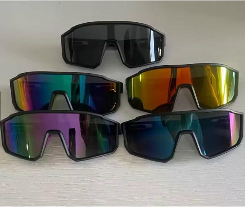 May include: Collection of sport sunglasses with black frames and various lens colors, including black, rainbow, orange, purple, and blue. The sunglasses have a modern, angular design, suitable for outdoor activities.