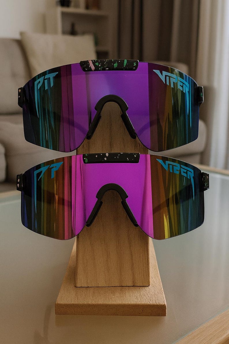 Puede incluir: Dos pares de gafas de sol Viper con lentes espejadas en tonos morados, azules y amarillos. Las gafas tienen monturas negras y la palabra "VIPER" est&aacute; impresa en las lentes. Se exhiben en un soporte de madera.