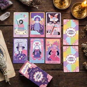 Op de afbeelding: Een Pastel Prism Tarot deck met geïllustreerde kaarten met grillige figuren en symbolen in pastelkleuren. Het deck bevat kaarten met de labels "Death", "Temperance", "Judgement", "The Magician", "The High Priestess" en "The Empress". De doos is paars met de tekst "Pastel Prism Tarot".