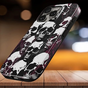 May include: A smartphone case featuring a repeating graphic pattern of white skulls set against a dark, deep red and black background. The case has precise cutouts for the camera lenses and side buttons, maintaining a sleek, protective profile.