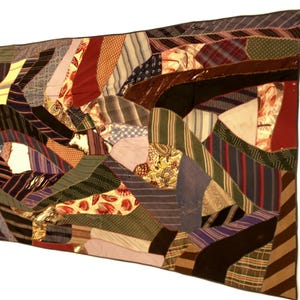 May include: A patchwork quilt with a variety of fabrics in shades of red, green, blue, and brown. The quilt is made of many different shapes and patterns, creating a unique and textured design. The quilt is rectangular and appears to be handmade.