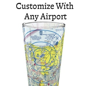 Peut inclure: Un verre à bière transparent orné d'une impression détaillée de carte aéronautique avec des couleurs jaune, bleue et blanche. Le texte Customize With Any Airport est imprimé au-dessus du verre. La carte inclut diverses données de navigation.