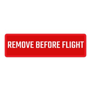 Könnte beinhalten: Ein rechteckiges rotes Stoffetikett mit weißem Rand und dem Text REMOVE BEFORE FLIGHT, der in fetten weißen Großbuchstaben in der Mitte aufgedruckt ist. Das Design ist flach und weist eine kontrastreiche Ästhetik auf rotem Grund auf.