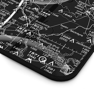 Könnte beinhalten: Eine schwarze, rechteckige Schreibtischunterlage mit einem detaillierten weißen Aufdruck einer Luftfahrtkarte. Die Karte zeigt verschiedene Navigationsmarkierungen, Flughafennamen wie Dunlea Airpark und numerische Höhendaten.