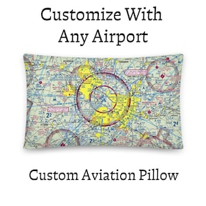 Puede incluir: Un cojín rectangular con un estampado detallado de una carta aeronáutica con marcas amarillas, azules y rojas. El texto Customize With Any Airport y Custom Aviation Pillow aparece encima y debajo del gráfico del cojín.