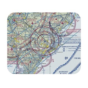 Puede incluir: Una alfombrilla de rat&oacute;n rectangular con una carta aeron&aacute;utica detallada de la regi&oacute;n de Atlantic City. El mapa muestra varias rutas de vuelo, &aacute;reas restringidas y datos de navegaci&oacute;n con etiquetas de texto que incluyen Atlantic City y Warning W-107C.