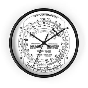 May include: A round wall clock with a black frame and a white face featuring the design of an E6-B flight computer. The dial displays various aviation scales, conversion formulas, and numerical markings in black text, with three black clock hands.