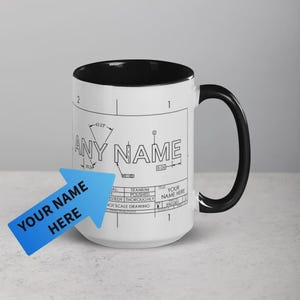 Op de afbeelding: Witte keramische mok met een zwarte binnenkant en handvat. De mok heeft een blauwdrukontwerp met de tekst "ANY NAME" en "YOUR NAME HERE". De mok heeft een standaardformaat voor koffie of thee.