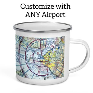 May include: A white enamel mug with a silver rim and handle, featuring a colourful aviation sectional chart of the Anchorage area printed on the side. Above the mug, the text reads: Customize with ANY Airport. The mug has a cylindrical shape.