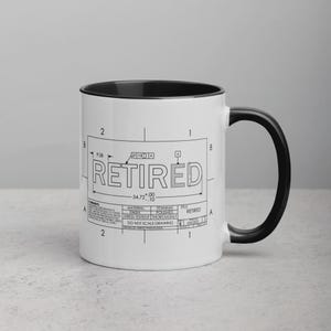 Puede incluir: Taza de cerámica blanca con interior y asa negros. La taza presenta un diseño tipo plano con la palabra "RETIRED" en un lugar destacado. El diseño incluye medidas y detalles técnicos, lo que le da una estética industrial.