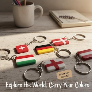 Puede incluir: Llaveros con banderas de varios países, como Suiza, Alemania e Inglaterra, con anillas plateadas. Los llaveros están colocados sobre una superficie de madera clara. El texto de la imagen dice: "¡Explora el mundo. ¡Lleva tus colores!" y "Adventure Awaits!"
