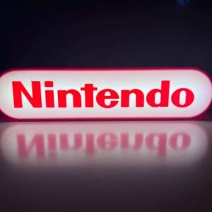 May include: A rectangular, illuminated sign with the word "Nintendo" in bold red letters. The sign has rounded edges and a white background, with a red border. The sign's reflection is visible below.