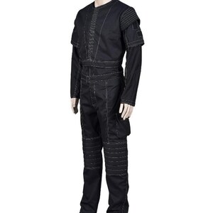 May include: Black jumpsuit with white stitching details. The outfit features a round neck, long sleeves, and a fitted waist. The pants have reinforced knee panels and pockets. The shoulders have a layered design.