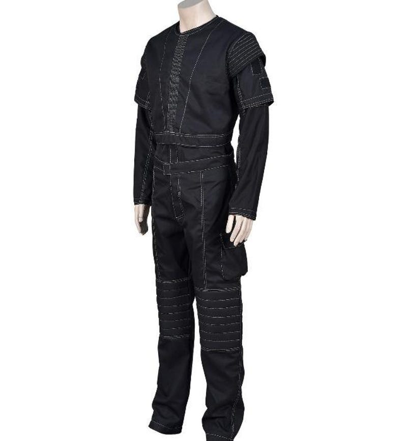May include: Black jumpsuit with white stitching details. The outfit features a round neck, long sleeves, and a fitted waist. The pants have reinforced knee panels and pockets. The shoulders have a layered design.