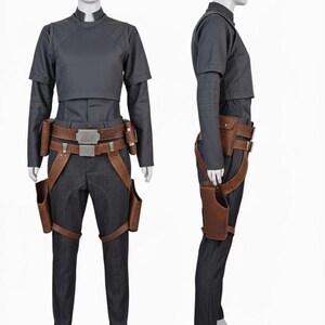 May include: A dark gray short-sleeved top and matching trousers worn with a brown leather utility belt featuring metallic buckles and two attached holsters. The ensemble includes a structured bodice overlay and fitted pants with a clean finish.