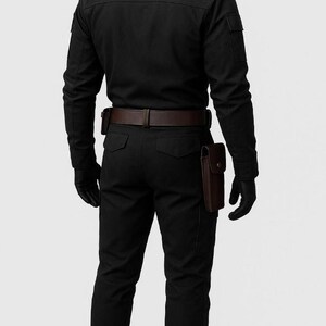Pu&ograve; includere: Una camicia nera a maniche lunghe e pantaloni neri abbinati indossati su un manichino. L'outfit include una cintura in pelle marrone scuro con una fondina e una tasca in pelle marrone separata fissata sul lato dei pantaloni. Guanti neri indossati.