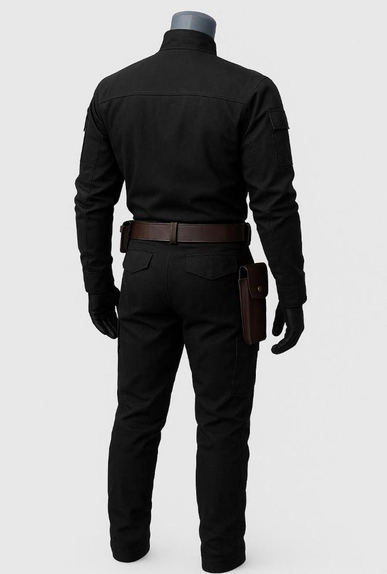 Pu&ograve; includere: Una camicia nera a maniche lunghe e pantaloni neri abbinati indossati su un manichino. L'outfit include una cintura in pelle marrone scuro con una fondina e una tasca in pelle marrone separata fissata sul lato dei pantaloni. Guanti neri indossati.