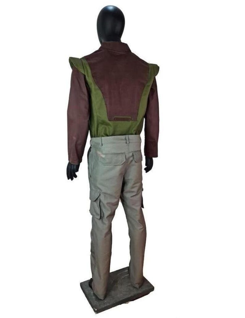 May include: A long-sleeved jacket featuring a dark brown upper section and a green lower panel with extended shoulder flaps, paired with light gray cargo pants. The outfit is displayed on a black mannequin against a plain white background.