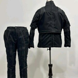 May include: A black two-piece outfit consisting of a jacket and trousers. The jacket features a high collar, short sleeves, and white contrast stitching. The trousers include matching white stitching and two rectangular pockets on the front thighs.