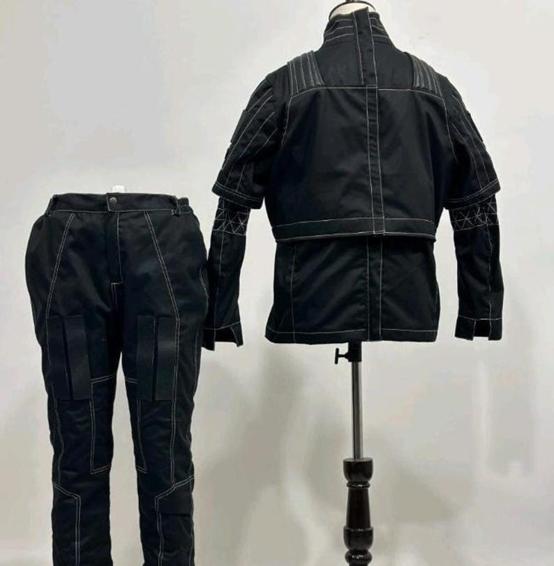 May include: A black two-piece outfit consisting of a jacket and trousers. The jacket features a high collar, short sleeves, and white contrast stitching. The trousers include matching white stitching and two rectangular pockets on the front thighs.