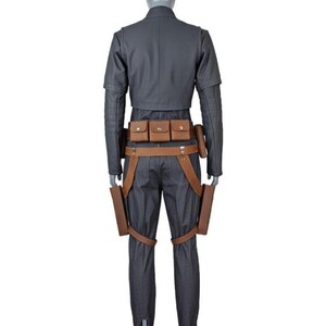 May include: A dark gray long-sleeved jacket and matching trousers worn on a mannequin. The outfit includes a brown leather utility belt with three small pouches and two holster-like attachments hanging down the sides of the legs.