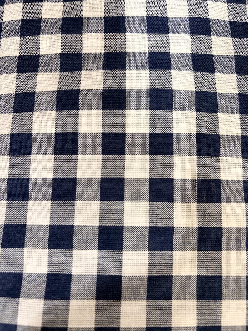 May include: A fabric featuring a classic gingham pattern with alternating dark navy blue and off-white squares. The textile displays a visible woven texture with a consistent grid design across the entire surface, creating a balanced checkerboard appearance.