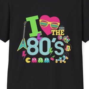 May include: Black t-shirt with a colorful graphic design that says "I Love the 80's". The design includes a guitar, a heart with sunglasses, and other 80s-themed icons like a boombox and roller skates.