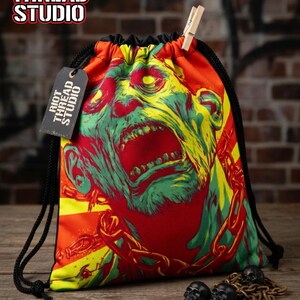 Puede incluir: Una bolsa con cordón con un diseño de zombi gritando en rojo, amarillo y verde. Tiene un cordón negro y una etiqueta con "Riot Thread Studio". El texto "ZOMBIE CHAIN SCREAM Drawstring Bag" está en la parte inferior.