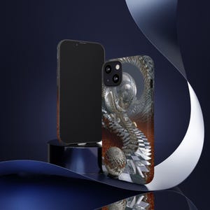 Op de afbeelding: Een zwarte smartphone en een telefoonhoesje met een gedetailleerd, abstract ontwerp. De hoes heeft een metallic, driedimensionaal kunstwerk met een dambordpatroon en een bol. De achtergrond is donkerblauw met een gebogen wit lint.