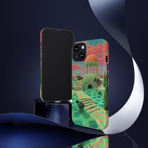 Op de afbeelding: Twee telefoonhoesjes. Eén is zwart, de andere heeft een kleurrijke illustratie van een gebouw met een oranje koepel, een brug en een groen landschap. De lucht is een mix van roze en blauw. De hoes zit op een zwarte standaard.