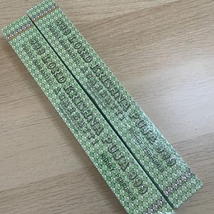 May include: Two rectangular incense boxes with green and white patterned designs. The boxes are labeled "999 LORD KRISHNA PUJA" and "HIGHLY PERFUMED". The boxes are lying on a light brown wooden surface.