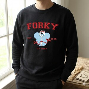 K&ouml;nnte beinhalten: Eine wei&szlig;e Keramiktasse mit schwarzem Henkel und dem Text "But First, Coffee" in fetter, schwarzer Schrift. Die Tasse steht auf einer Holzoberfl&auml;che. Die Tasse ist etwa 10 cm hoch.