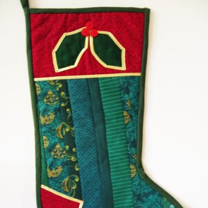 Peut inclure: Une chaussette de Noël rouge et verte avec un motif de houx. La chaussette est faite de tissu patchwork avec une variété de motifs et de textures.