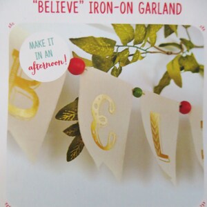 Może przedstawiać: Biały baner z płótna z pozłacanymi literami, na którym widnieje napis "BELIEVE", oraz zieloną i czerwoną koralikiem. Baner jest częścią girlandy, którą można zrobić w ciągu jednego popołudnia.