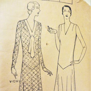 May include: A vintage sewing pattern for a dress with two different views. The first view shows a dress with a geometric pattern and a bow at the neckline. The second view shows a simple dress with a V-neckline. The pattern includes the text "VIEW 1" and "VIEW 2".