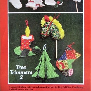 May include: A set of five Christmas tree ornaments, including a stocking, a 3-D tree, a candle, and a hobby horse. The ornaments are made of fabric and are decorated with various patterns and colors. The text "Tree Trimmers 2" is printed on the page.